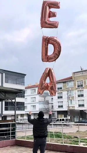 Rose gold harfli isim zinciri Bir kişinin iki eliyle tuttuğu rose gold harf balonu zinciri, arkasında şehir manzarası